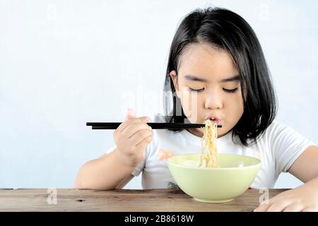 Asiatische Mädchen bläsen Instantnudeln mit viel Appetit. Mit ihrem Schweiß auf der Stirn wirkt sie niedlich und appetitlich, ein glückliches Kind. Stockfoto