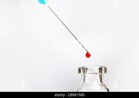 Fläschchen und Spritzennadel mit Tropfen roter Flüssigkeit. Stockfoto