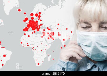 Blonde Erwachsene Frau von 50-60 Jahren in einer medizinischen Maske und einer Weltkarte mit Epidemieausbrüchen auf grauem Hintergrund. Konzept Zum Schutz Vor Virus-Pandemie Stockfoto