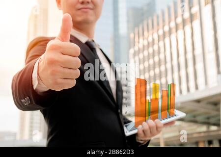 Geschäftsleute halten sich an den Daumen, um Freude auszudrücken. Wenn Sie das Tablett halten und es die Diagrammdaten anzeigt, die von der Grafik generiert werden, über erfolgreiche Flosse Stockfoto