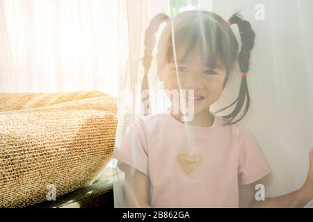 Lernen vom Spielkonzept. Sehr süßes Mädchen, das heimlich spielt, schleicht sie sich in die Vorhänge. Sie wartet darauf, dass die Menschen sie finden. Stockfoto