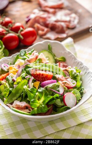 Frischer Frühlingssalat mit grünen Blättern Tomaten eiriger roter Zwiebel junger Erbsen Prosciutto Feta Käse und Olivenöl Stockfoto