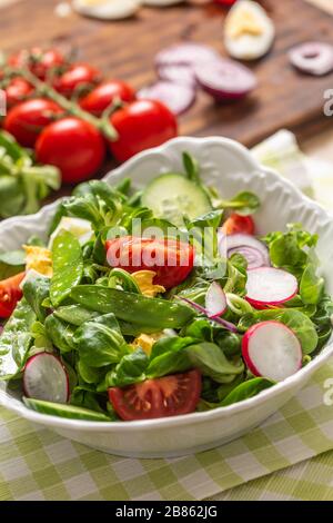 Frischer Frühlingssalat mit grünen Blättern Tomaten eiriger roter Zwiebel junger Erbsen Prosciutto Feta Käse und Olivenöl Stockfoto