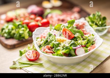 Frischer Frühlingssalat mit grünen Blättern Tomaten eiriger roter Zwiebel junger Erbsen Prosciutto Feta Käse und Olivenöl Stockfoto