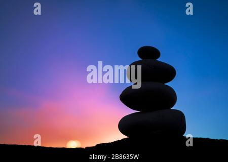 Die zusammengestapelten Steine sind vergleichbar mit der Yoga-Meditation. Hintergrund ist Abendhimmel, leuchtende Farben sind gute Energie. Ausgeglichen, leistungsbereit Stockfoto