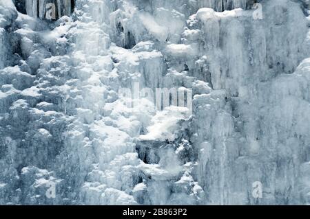 Ein kleiner Bergwasserfall zwischen Eis und Schnee. Hintergrund, kalte Farbtöne, Winterlandschaft Stockfoto