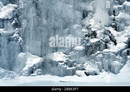 Ein kleiner Bergwasserfall zwischen Eis und Schnee. Hintergrund, kalte Farbtöne, Winterlandschaft Stockfoto