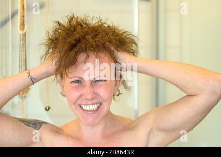Frustrierte Frau, die einen schlechten Haartag hat, der ihre Hände durch ihr unruly lockiges Haar führt und in einem Nahkopfschuss schreit Stockfoto