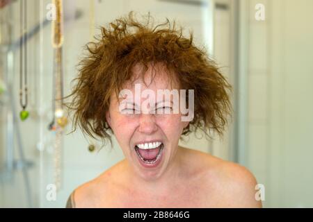 Frau, die an einem schlechten Haartag frustriert schreit und nach dem Duschen in einem Nahporträt ihre unbeweglichen lockigen Haare in alle Richtungen fliegen Stockfoto