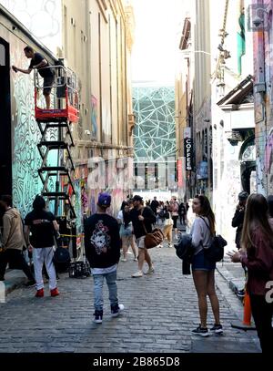 Ein Straßenkünstler arbeitet in Hosier Lane, Melbourne, während Besucher an der mit Graffiti beladenen schmalen Straße vorbeifahren Stockfoto