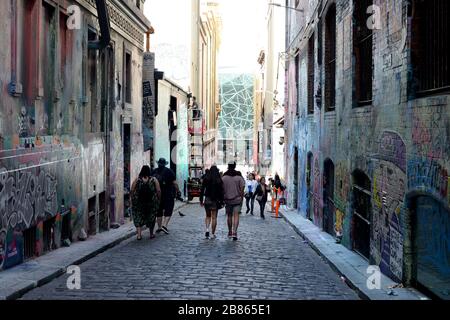Ein Straßenkünstler arbeitet in Hosier Lane, Melbourne, während Besucher an der mit Graffiti beladenen schmalen Straße vorbeifahren Stockfoto