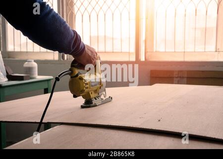 Nahaufnahme eines Tischlers mit einer elektrischen Säge zum Schneiden eines großen Holzblattes. Stockfoto