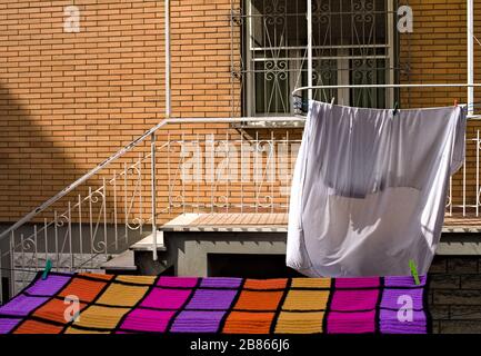 Weiße Bettlaken und eine bunte Decke, die auf dem Wäschestüß vor dem Balkon hängen (Pesaro, Italien, Europa) Stockfoto