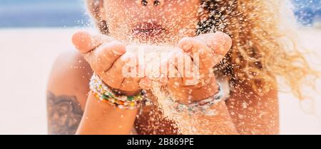 Nahaufnahme des schönen kaukasischen Wmoan, der Sand aus den Händen am Strand bläst - Reise- und Sommerferienkonzept - konzentrieren Sie sich auf Sand und Unschärfe Stockfoto