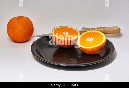 Standzeit einer geschnittenen Orange auf einer schwarzen Platte mit weißem Hintergrund Stockfoto