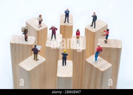 Miniaturspielzeuge, die auf Holzklotz stehen - soziale Distanzierung, anti-soziales Konzept oder Teamarbeit. Stockfoto