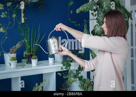 Ein Mädchen in wunderschöner Kleidung bewässert die Blumen in der Halle aus einer metallenen Gießkanne. Stockfoto