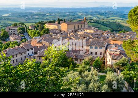 Chiesa di Sant'Agostino und Dächer des historischen Zentrums von San Gimignano von der Rocca di Montestaffoli im Parco della Rocca bei Sonnenuntergang. Stockfoto