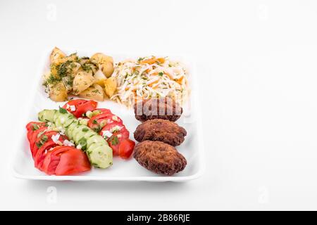 Gebratene Fleischbällchen mit Salat und Kartoffeln in einem Teller auf weißem Hintergrund Stockfoto