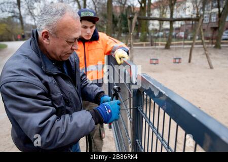 Berlin, Deutschland. März 2020. Osman Türker (l) und Nils Willimsohn, beide Gärtner im Park-Department von Charlottenburg-Wilmersdorf, sperren einen Spielplatz im Volkspark Wilmersdorf mit Draht. Um die Ausbreitung des Corona-Virus zu verlangsamen, hat die Bundesregierung das öffentliche Leben erheblich eingeschränkt. Credit: Christoph Soeder / dpa / Alamy Live News Stockfoto