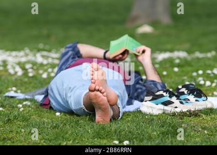 20. März 2020, Hessen, Frankfurt am Main: Ein Mann liest bei sonnigem Frühlingswetter ein Buch auf einer Wiese im Frankfurter Günthersburgpark. Foto: Arne Dedert / dpa Stockfoto