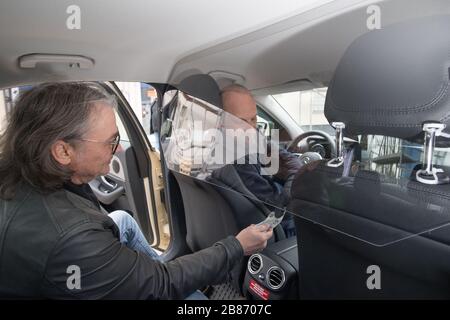 Berlin, Deutschland. März 2020. Taxifahrer Volker nimmt einen Bankschein unter einem Schutzschirm an. Die Schutzscheibe soll Fahrer und Beifahrer vor dem Coronavirus schützen. Kredit: Jörg Carstensen / dpa / Alamy Live News Stockfoto