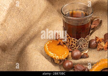 Ein Glas Tee in einem Vintage-Cup-Halter, Plätzchen und Schokolade auf einem Hintergrund aus strukturiertem Stoff. Nahaufnahme Stockfoto