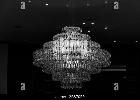 Schwarz-Weiß-Stock Foto von Kronleuchter mit funkelnden Glasbehängen auf dunklem Hintergrund. Geometrische Form symmetrische moderne Lampe Nahaufnahme. Glänzende Lampe Stockfoto
