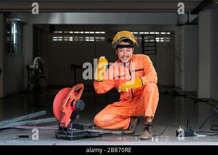Der Stahlarbeiter posiert selbstbewusst an seinem Arbeitsplatz. Metallschleifen auf Stahlersatzteil in der Werkstatt. Trennschneiden und Schweißen von Metall durch Industriearbeiter. Stockfoto
