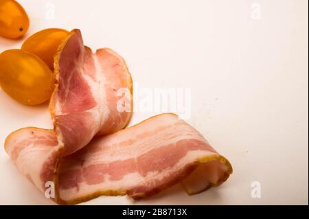 Speckscheiben und Tomaten auf weißem Hintergrund. Nahaufnahme Stockfoto