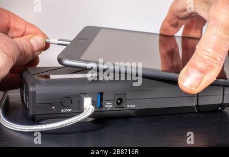 Man's Hands Verbinden Sie das Ladekabel eines Tablet-Computers mit einem USB-Anschluss eines kompakten und tragbaren Akku-Netzteils/Ladegeräts. Stockfoto