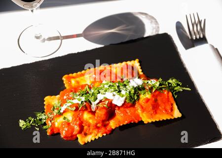 Vier mit Käse gefüllte Ravioli in Tomaten- und Basilikumsoße auf dem schwarzen Steinteller, einem berühmten Gericht aus der französischen Stadt Nizza Stockfoto