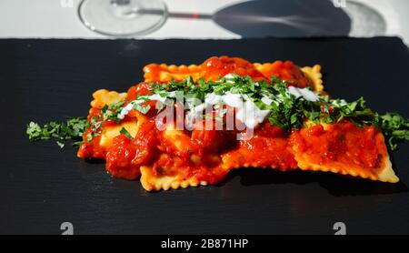 Vier mit Käse gefüllte Ravioli in Tomaten- und Basilikumsoße auf dem schwarzen Steinteller, einem berühmten Gericht aus der französischen Stadt Nizza Stockfoto