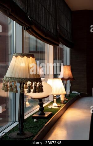 Fensterbank mit verschiedenen antiken Lampen und Vintage-Lampenschirm mit Quasten am unteren Rand im Vordergrund. Innenbeleuchtungskonzept mit verschiedenen Lampen. Stockfoto