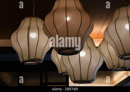 Nahaufnahme von Pendelleuchten im Retro-Design mit traditionellen chinesischen Lampenschirmen, die unter der Decke hängen. Glasflächen von Lampen mit glühenden Glühbirnen Stockfoto