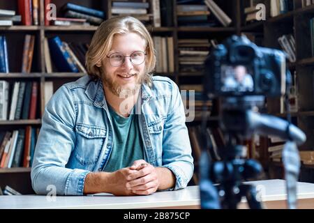 Lächelnder junger männlicher Schöpfer Blogger, der über Aufnahmen mit professioneller Kamera spricht. Stockfoto