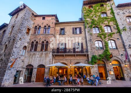 San Gimignano, Toskana: In der Abenddämmerung genießen die Gäste ihr Abendessen und den Wein der Region im Freien im Restaurant Hotel la Cisterna auf der Piazza della Cisterna. Stockfoto