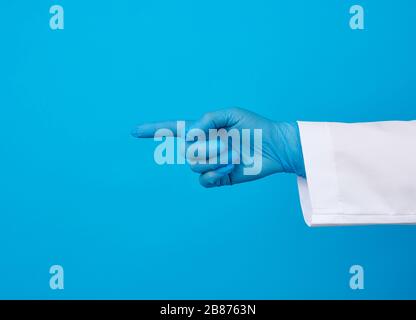 medic Frau in weißem Mantel, mit blauen sterilen Handschuhen, mit Handgeste, die auf das Motiv hinweist, blauer Hintergrund Stockfoto