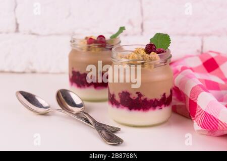 Zwei Portionen Schoko-Vanille-Pudding mit Beeren und einem Glas auf weißem Hintergrund. Stockfoto