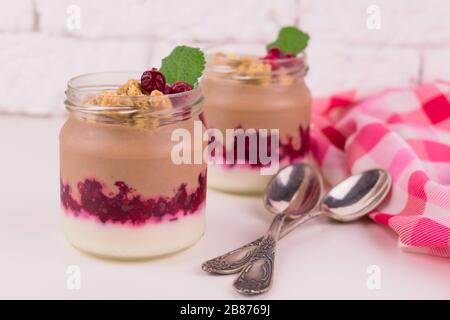 Zwei Portionen Schoko-Vanille-Pudding mit Beeren und einem Glas auf weißem Hintergrund. Stockfoto