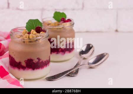 Zwei Portionen Schoko-Vanille-Pudding mit Beeren und einem Glas auf weißem Hintergrund. Stockfoto