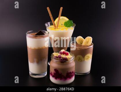 Schokolade-Vanille-Dessert (Pudding) in verschiedenen Gläsern auf schwarzem Hintergrund. Stockfoto