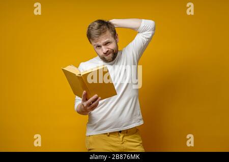 Der nachdenkliche bärtige Mann hält ein Buch in Händen, das er bis in die Mitte gelesen hat und nun Widersprüche erlebt. Stockfoto