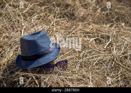 Blauer Hut und Sonnenbrille auf trockenem Strohhalm am Standort des Landes Stockfoto