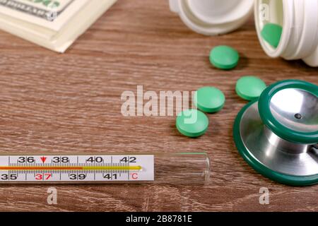 Hohes Fieber ist das erste Anzeichen einer Coronavirus-Infektion oder Covid-19. Stethoskop, Pillen, Thermometer mit hohem Fieber und Dollarstapel auf Holztisch. C Stockfoto