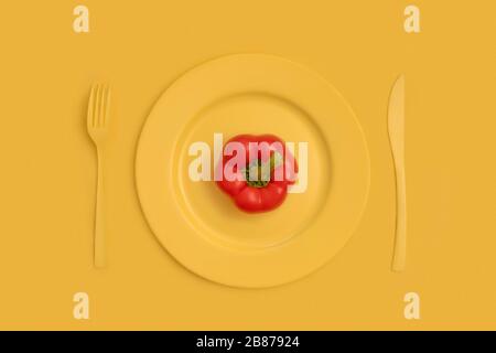 Rote Paprika oben auf gelber Platte, Messer und Gabel. Auf gelbem Hintergrund. Die Ansicht von oben. Stockfoto