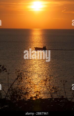 Ein Boot, das durch die Unterstellung der untergehenden Sonne in der Nähe von Hunstanton an der Küste von West Norfolk segelt Stockfoto