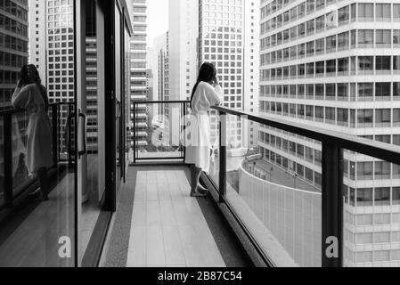 Junge, schöne asiatische Frau, die vom Balkon aus den Blick auf die Stadt genießt Stockfoto