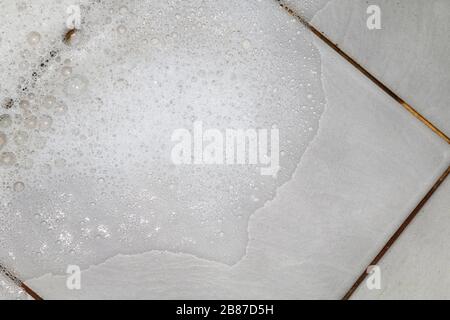 Seifenlauge mit Seifenlauge und Scheuern des Badezimmerbodens Schmutz nass, Schaumstoff weiße Seifenblase aus Shampoo waschen auf Fliesen Boden Draufsicht Stockfoto