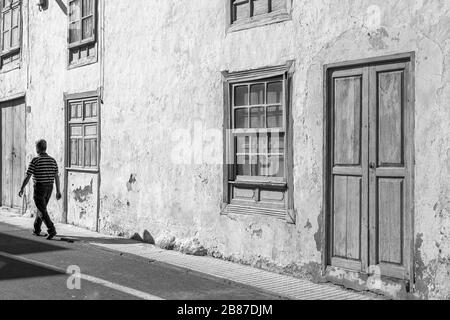 Ein Mann spaziert an interessanten alten Gebäuden und Häusern in der historischen Altstadt von Guia de Isora, auf Tenera, auf den Kanarischen Inseln, in Spanien vorbei Stockfoto